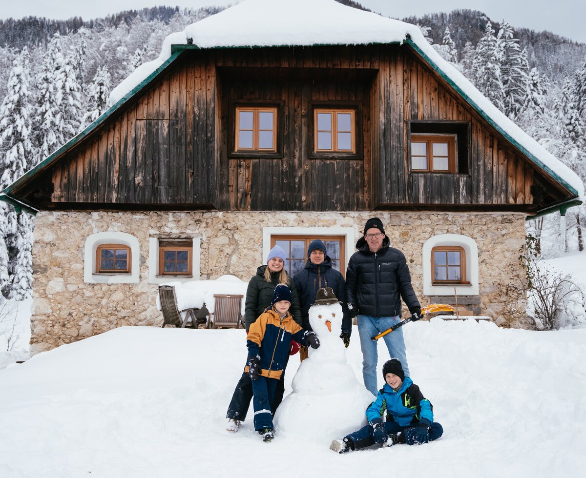 Gemeinsam Schneemannbauen | © Daniel Gollner / Urlaub am Bauernhof Kärnten Familie steht bei Schneemann vor Hütte | © Daniel Gollner / Urlaub am Bauernhof Kärnten