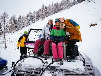 Anreise mit dem Pistengerät zur Bergfriedhütte am Millstättersee, Kärnten | © Urlaub am Bauernhof Kärnten/ Daniel Gollner Group of people in winter outfits taking a selfie on a snow-covered mountain path, seated on a snow vehicle. | © Urlaub am Bauernhof Kärnten/ Daniel Gollner