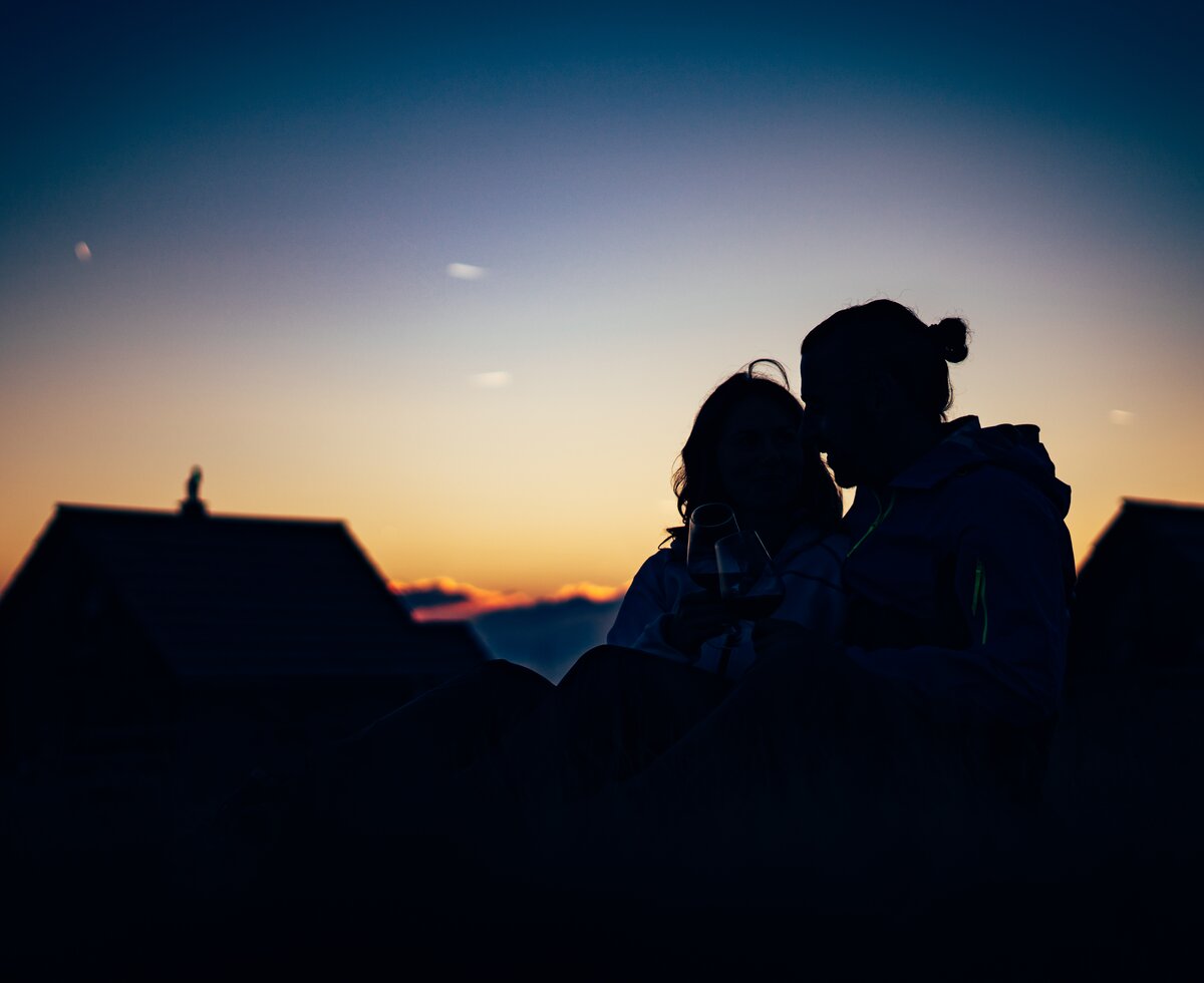 Paar im Sonnenuntergang vor der Almhütte Paar sitzt im Gras im Sonnenuntergang vor der Almhütte