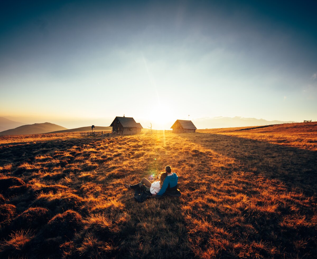 Paar sitzt vor der Hütte im Gras und genießt den Sonnenuntergang auf der Alm | © Urlaub am Bauernhof Kärnten/ Daniel Gollner 