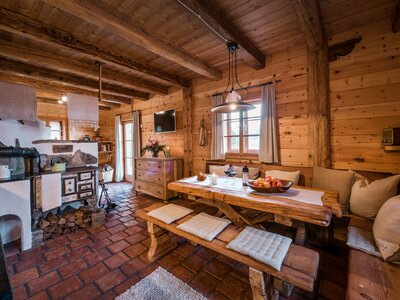 Blick ins Bergchalet Moseralm | © Günter Standl Cozy wooden cabin interior with rustic furnishings, fireplace, and dining area displaying fruits and flowers. | © Günter Standl
