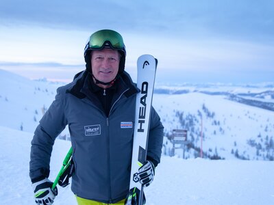 Franz Klammer | © BRM / Mathias Prägant Skifigur in Winterkleidung, haltend Ski und Stöcke, vor verschneiter Berglandschaft mit Skiliften im Hintergrund. | © BRM / Mathias Prägant