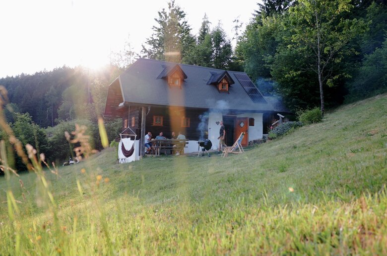 Auf einer idyllischen Almhütte umgeben von Wiesen und Wäldern wird gemeinsam gegrillt. Freunde sitzen auf der Veranda zusammen und reden. | © Urlaub am Bauernhof / Daniel Gollner