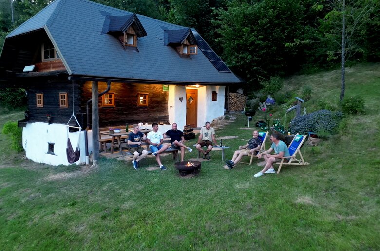 6 Freunde sitzen bei sommerlicher Abendstimmung vor der Almhütte rund um ein knisterndes Lagerfeuer in einer Feuerschale. | © Urlaub am Bauernhof / Daniel Gollner