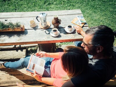 Zwei Personen genießen Kaffee und Lektüre auf einer hölzernen Terrasse inmitten einer grünen Umgebung. | © Urlaub am Bauernhof Steiermark / Daniel Gollner 