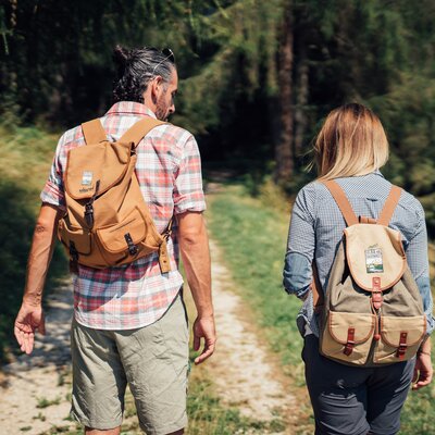 Two hikers with backpacks walking on a path in a lush, forested area. | © Urlaub am Bauernhof Steiermark / Daniel Gollner 
