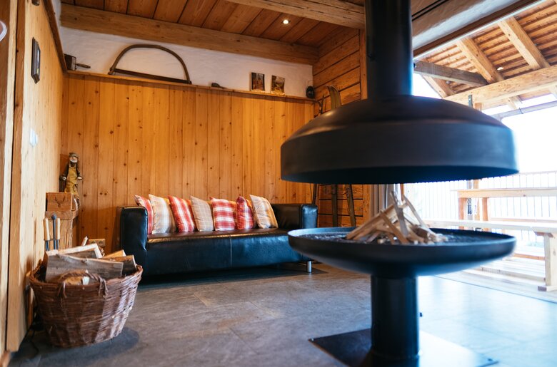 Gemütliches Holzhütten-Interieur mit Sofa, Kaminofen und Holzkörben. Ein modernes, rustikales Ambiente, das zu einem entspannenden Aufenthalt einlädt. | © Urlaub am Bauernhof Steiermark / Daniel Gollner