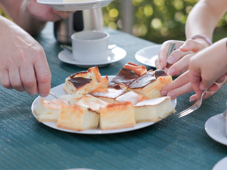 People sharing slices of cake outdoors at a social gathering, with tea or coffee on the table.