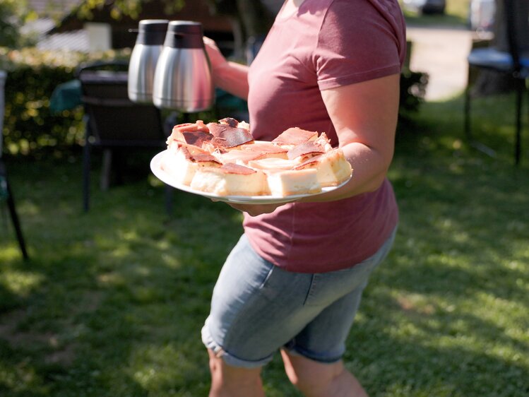 Person holding a tray with drinks and snacks outdoors in the sunlight.