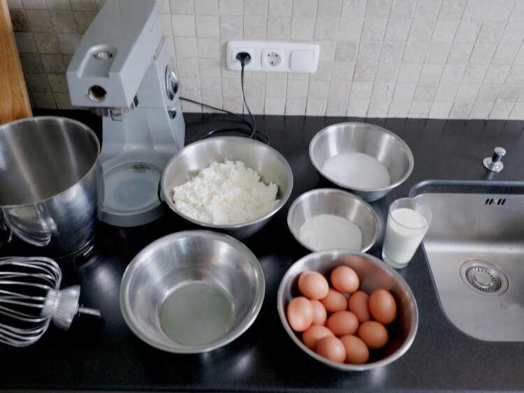 Küchenarbeitsplatz mit Mixer, Schüsseln mit Mehl, Zucker, Wasser, Milch, Eiern, und eine Küchenwaage, benutzerbereit zum Backen.