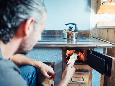 Mann heizt den Ofen mit Holz ein | © Urlaub am Bauernhof Steiermark / Daniel Gollner