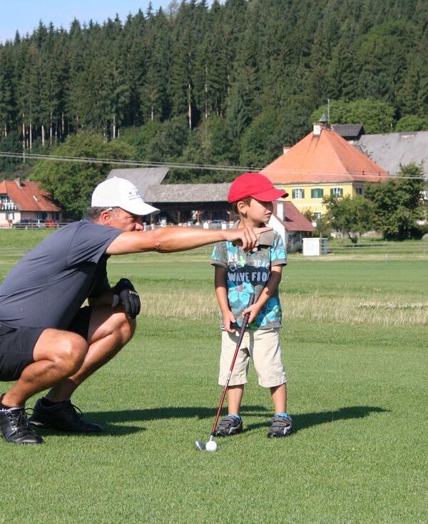 Mann zeigt dem Bub etwas beim Golf spielen | © Urlaub am Bauernhof Kärnten