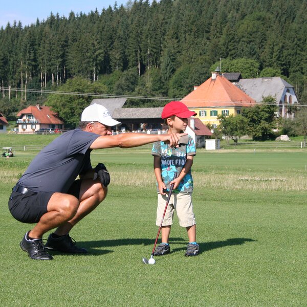 Mann zeigt dem Bub etwas beim Golf spielen | © Urlaub am Bauernhof Kärnten