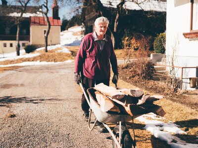 Bäuerin fährt mit dem Holz in der Scheibtruhe | © Urlaub am Bauernhof Kärnten / Daniel Gollner