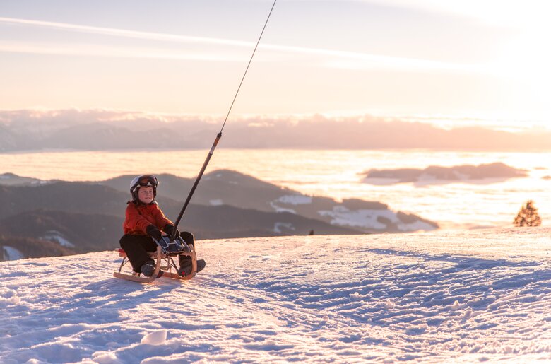 Winterspaß auf der Saualpe | © Michael Stabentheiner / Tourismusregion Mittelkärnten Kind auf Schlitten im Abendlicht im Schnee | © Michael Stabentheiner / Tourismusregion Mittelkärnten