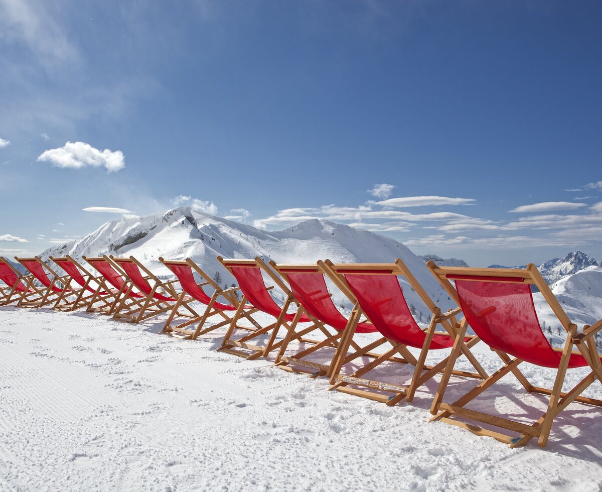 Liegestühle aufgereiht in der Sonne im Hintergrund das Skigebiet Nassfeld | © Martin Steinthaler - Kärnten Werbung GmbH