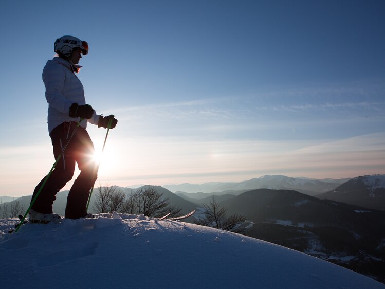 Female skier stands on summit at sunrise