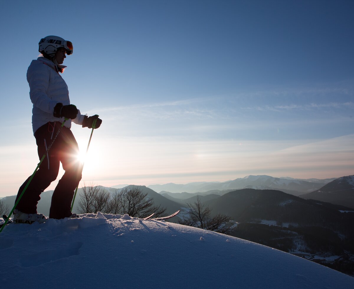 Female skier stands on summit at sunrise