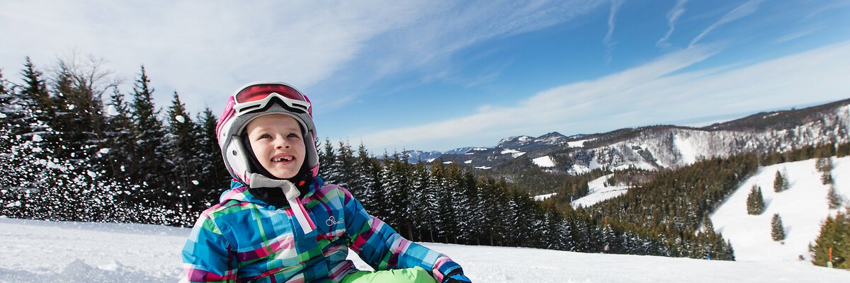 Kind sitzt mit Ski auf der Piste | © Niederösterreich Werbung / schwarz-koenig.at