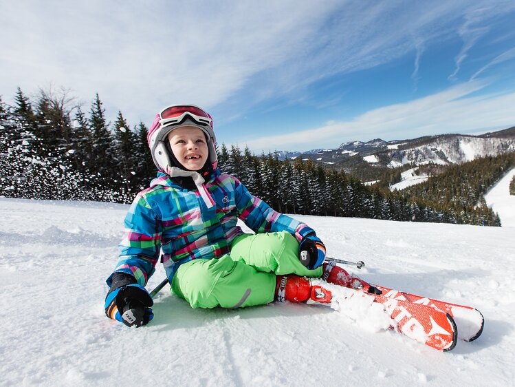 Child sits with skis on the slope | © Niederösterreich Werbung / schwarz-koenig.at