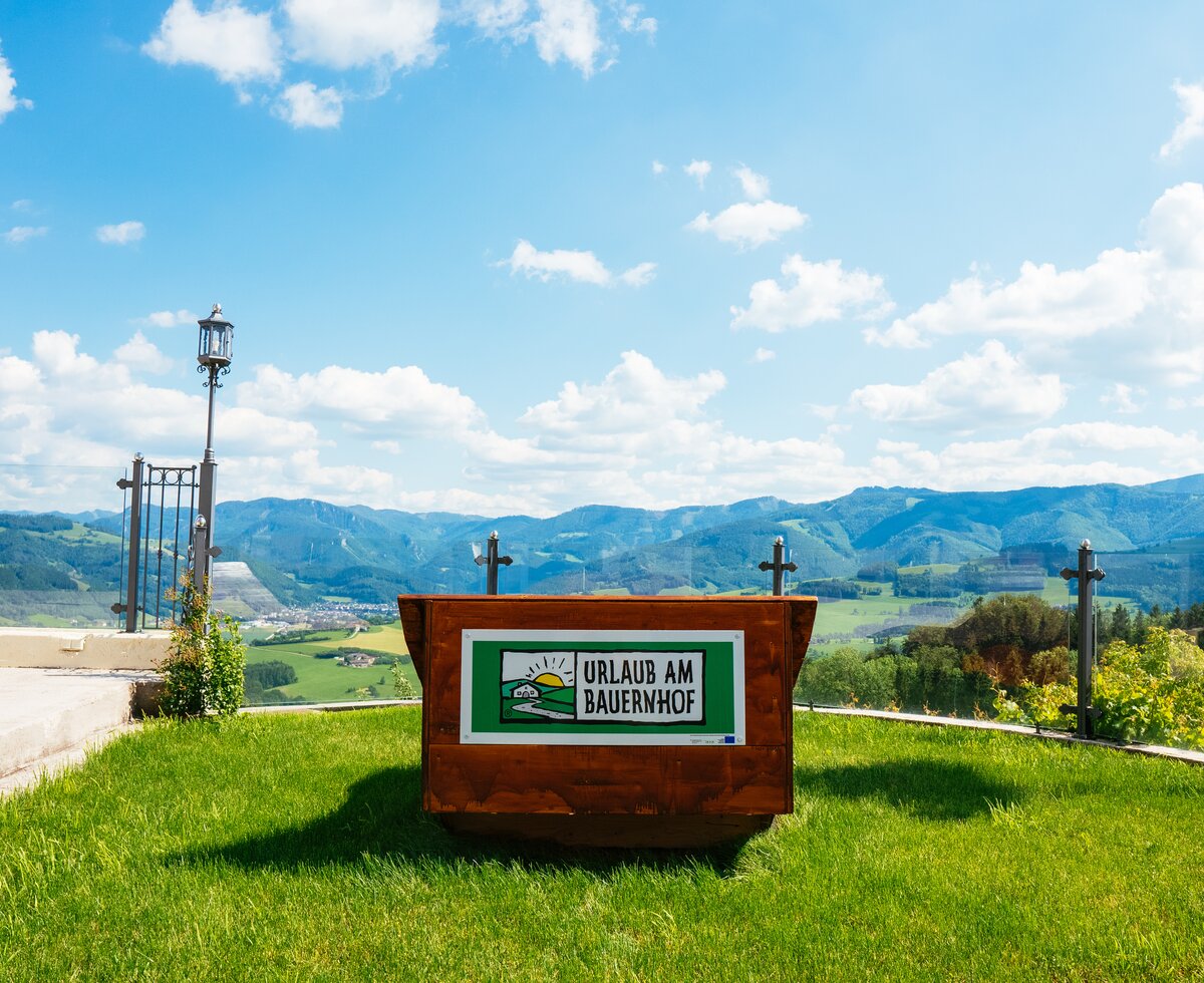 Liege mit der Aufschrift "Urlaub am Bauernhof" und Panoramablick auf den Nationalpark Kalkalpen | © Urlaub am Bauernhof Oberösterreich / Daniel Gollner