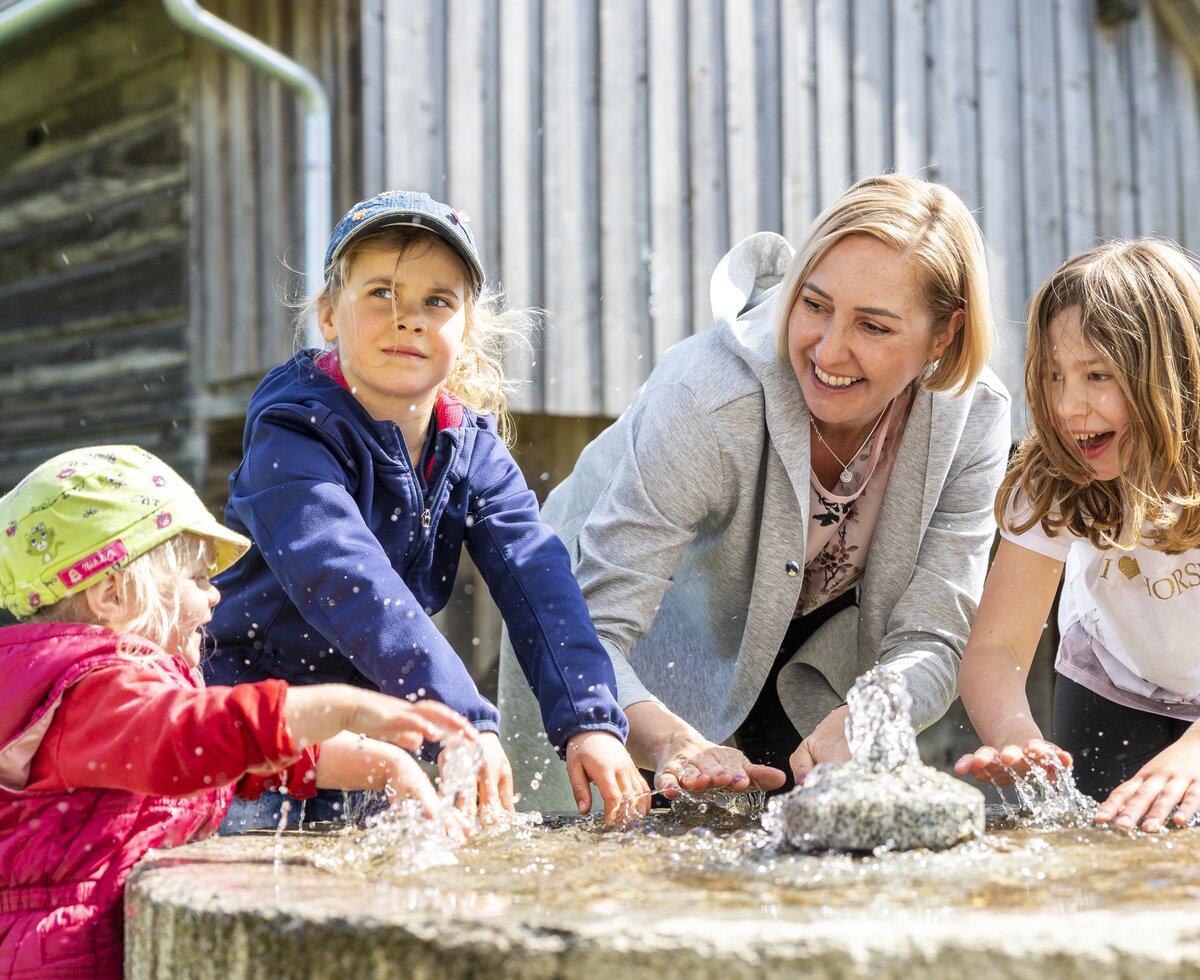 Mama und Kinder plantschen an einem Brunnen | © Urlaub am Bauernhof Oberösterreich / Puremotions Photography