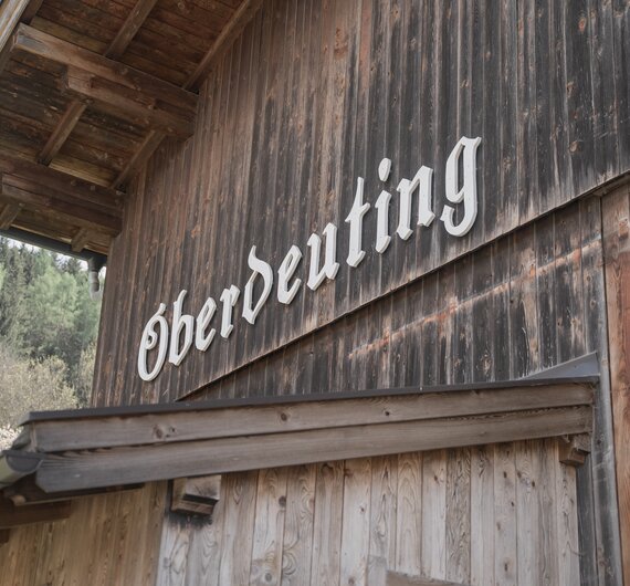 Ein uraltes, verwittertes Holzgebäude mit einem geschnitzten Schriftzug "Eberdutting" auf der Fassade vor einer bewaldeten Landschaft. | © Urlaub am Bauernhof / Daniel Gollner
