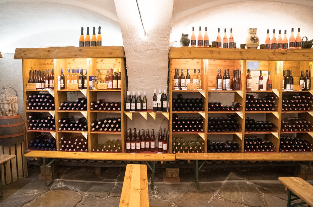 Holzregale mit zahlreichen Weinflaschen in verschiedenen Größen und Farben. Auf den Regalen sind auch einige andere Spirituosen ausgestellt. Der Raum erscheint dunkel und gemütlich. | © Urlaub am Bauernhof / Daniel Gollner
