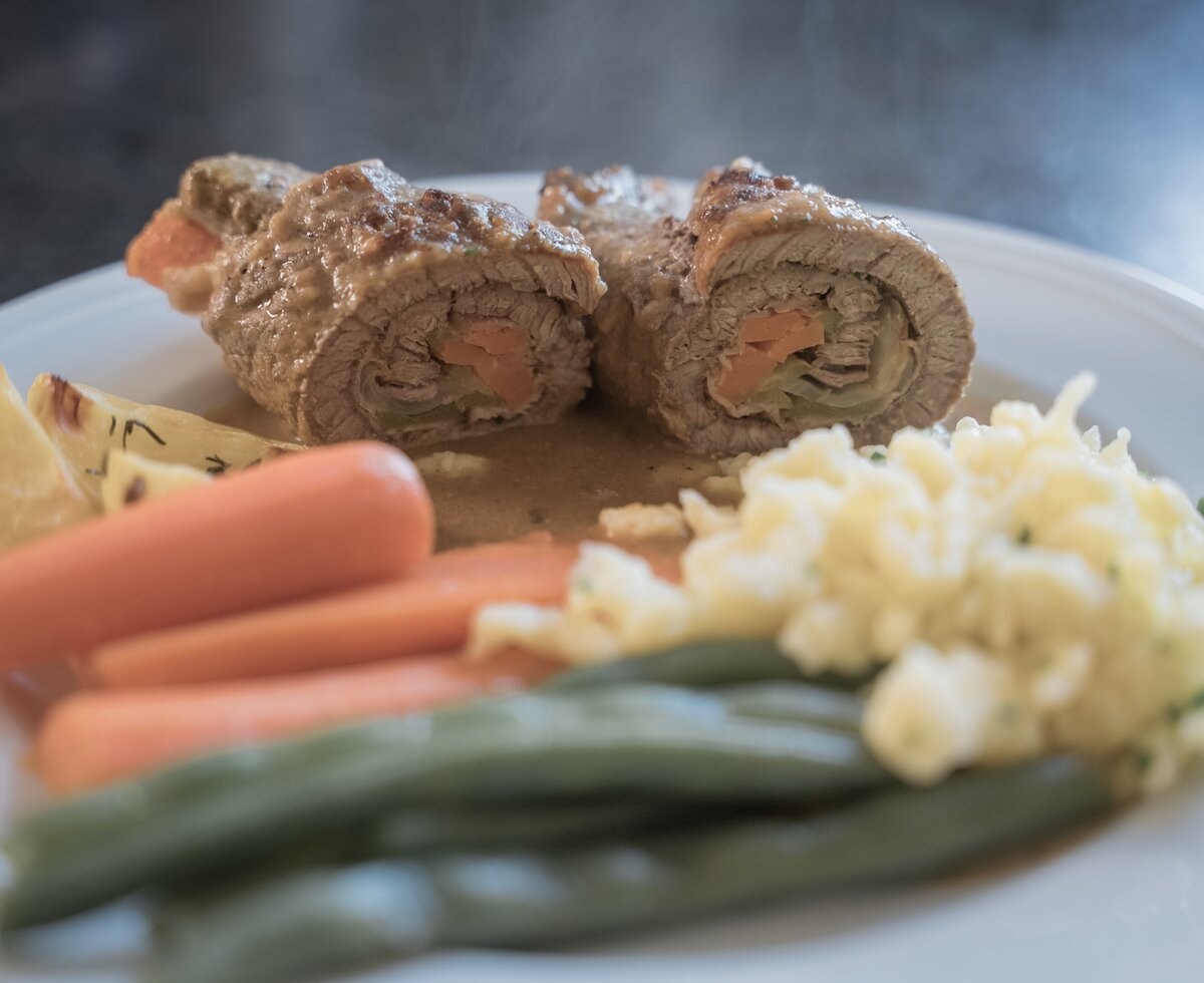 Ein mit Soße belegter Fleischrollbraten, serviert mit weißen Kartoffeln, Karotten und grünen Bohnen auf einem Teller. | © Urlaub am Bauernhof / Daniel Gollner