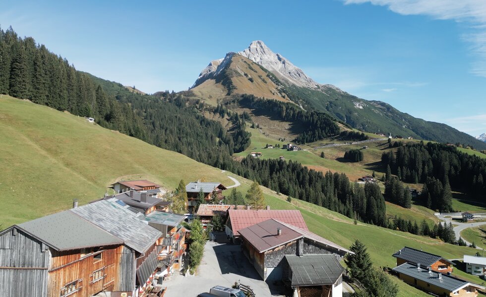 Idyllisches Bergdorf umgeben von steilen Gipfeln, grünen Wiesen und Wäldern. Traditionelle Holzhäuser und Ferienwohnungen in einer atemberaubenden alpinen Landschaft.
