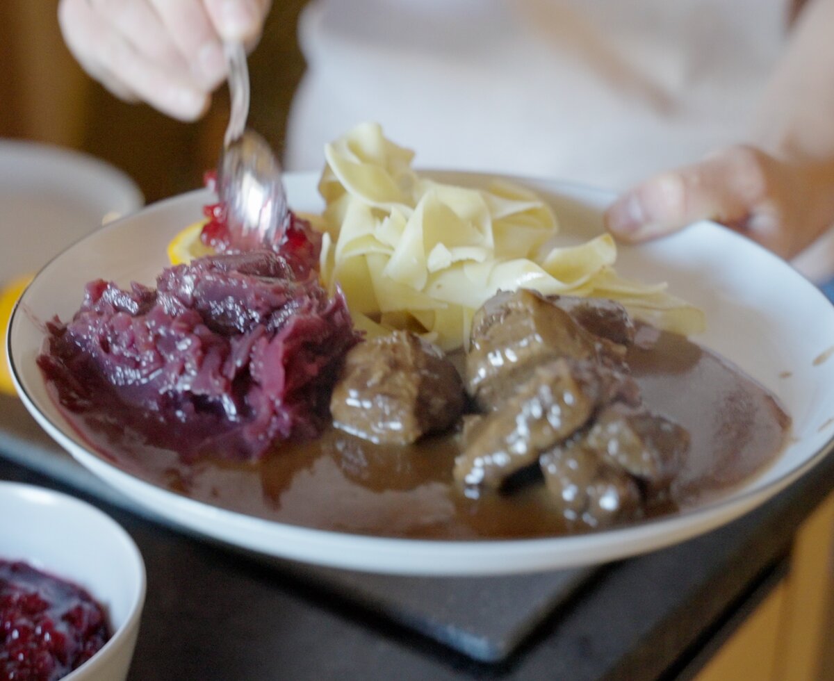 Teller mit geschmortem Fleisch, Kartoffeln und rotem Krautsalat. Eine Gabel mischt die Speisen. Eine leckere, deftige Mahlzeit, die appetitlich aussieht. | © Urlaub am Bauernhof / Daniel Gollner