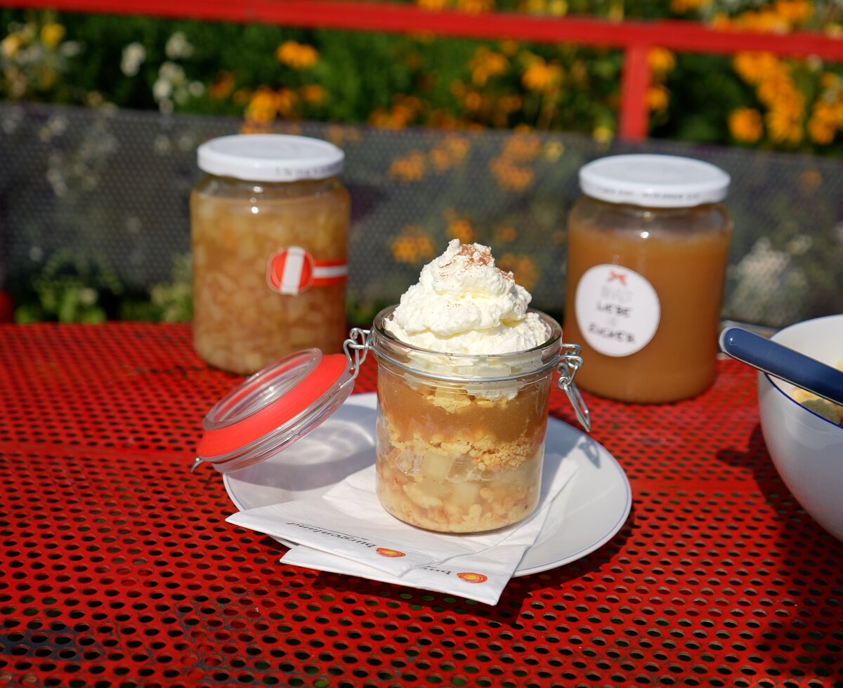 Verschiedene hausgemachte Konserven und Desserts auf einem roten Klapptisch in einer malerischen Umgebung mit Blumen. | © Urlaub am Bauernhof / Daniel Gollner