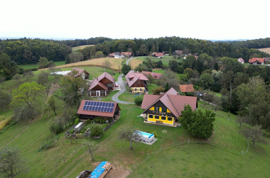 Ländliche Landschaft mit Holzhäusern, Gärten, Pool und Solarplatten, eingebettet in sanfte Hügel und Wälder. | © Urlaub am Bauernhof / Daniel Gollner