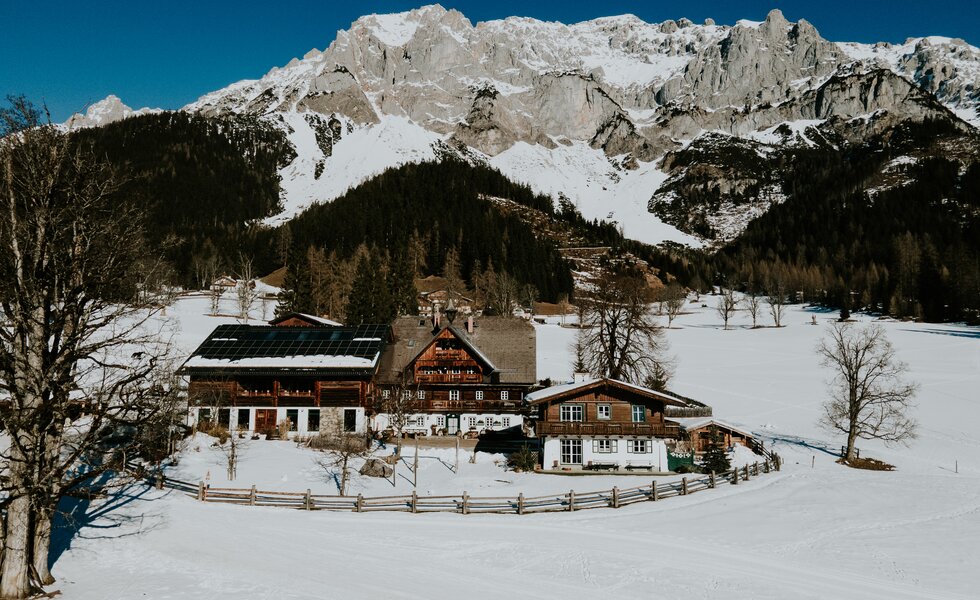 Dorfplatz in einer verschneiten Winterlandschaft mit Bergen im Hintergrund, bestehend aus Holzhäusern mit Schneebedeckten Dächern. | © Urlaub am Bauernhof / Daniel Gollner