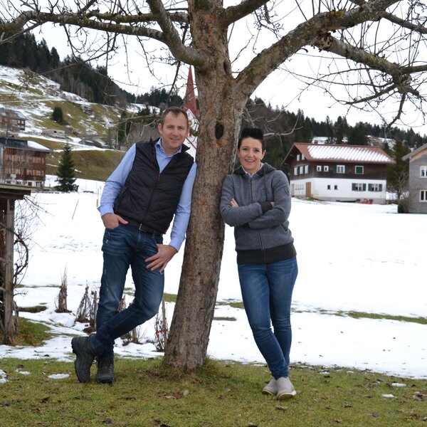 Bauer und Baeuerin lehnen am Baum vor verschneiter Wiese | © Urlaub am Bauernhof Österreich / Dorner