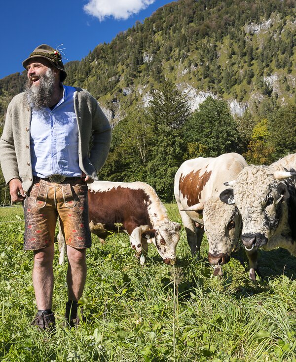Bauer lacht auf der Wiese bei den Kühen | © Urlaub am Bauernhof / Uwe Grinzinger