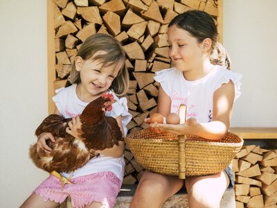 Zwei Mädchen mit Huhn und Eier | © Urlaub am Bauernhof / Oststeiermark Tourismus / Bernhard Bergmann Zwei Mädchen sitzen mit einem Huhn und Eiern auf der Hausbank | © Urlaub am Bauernhof / Oststeiermark Tourismus / Bernhard Bergmann