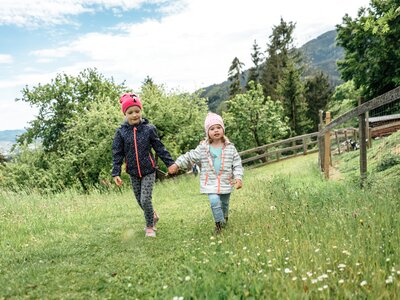 Zwei Mädchen wandern händchenhaltend durch die Wiese | © Urlaub am Bauernhof / Daniel Gollner