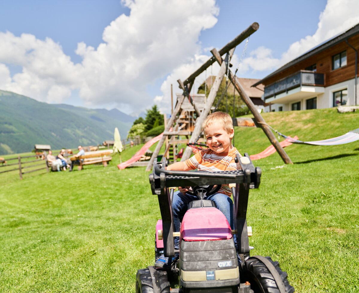 Bub fährt mit Spielzeugtraktor am Spielplatz | © Urlaub am Bauernhof / Punkt und Komma Bub fährt mit einem Spielzeugtraktor auf dem Spielplatz | © Urlaub am Bauernhof / Punkt und Komma