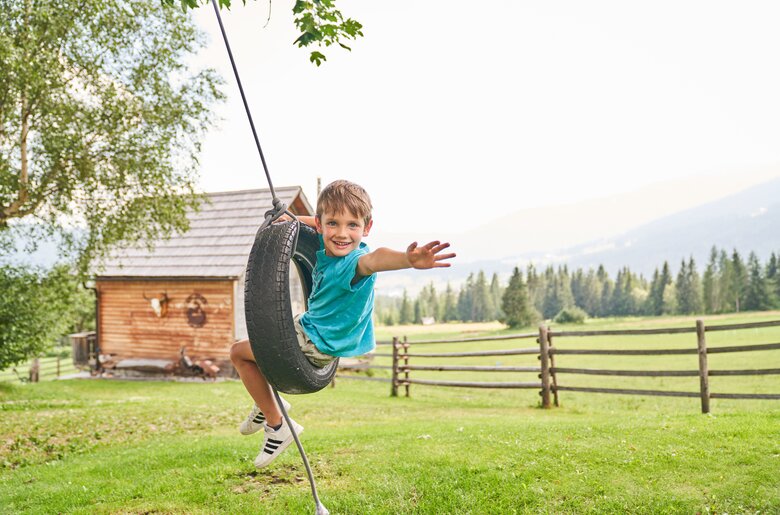Kind schaukelt in einem Reifen | © Urlaub am Bauernhof / Punkt und Komma