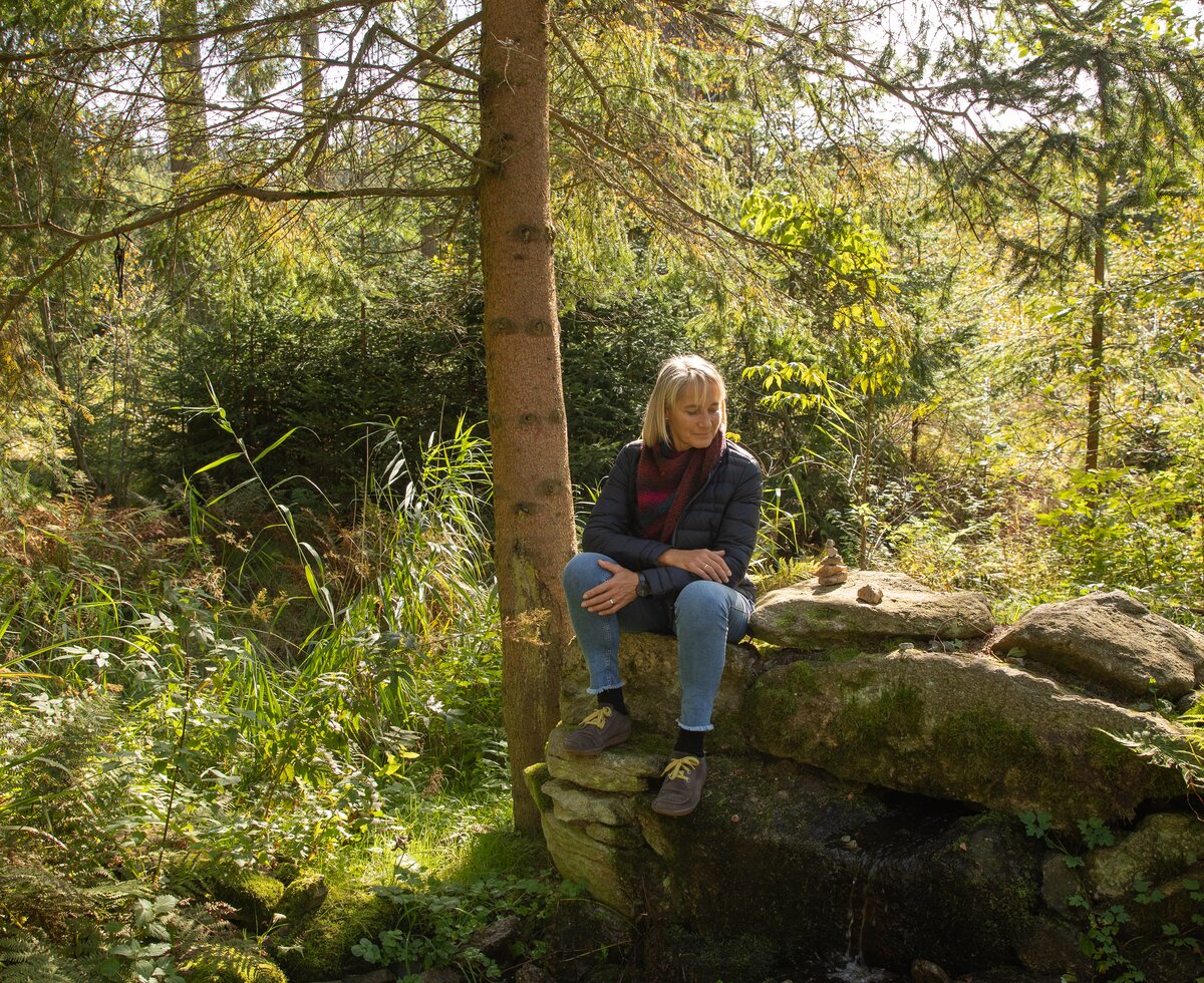 Frau sitzt auf einem Stein im Wald | © Urlaub am Bauernhof / Punkt und Komma