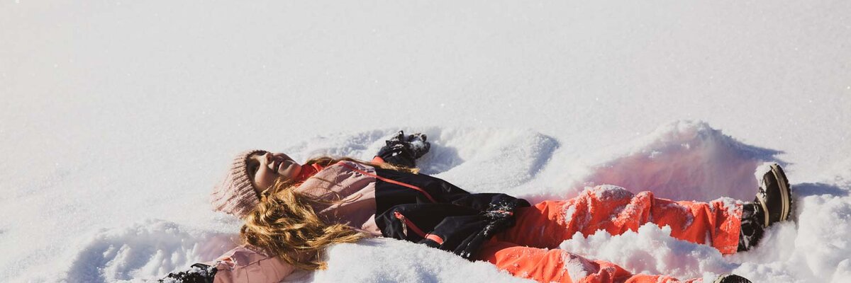 Mädchen mit buntem Schianzug macht Schneeengel | © Urlaub am Bauernhof / Pascal Baronit