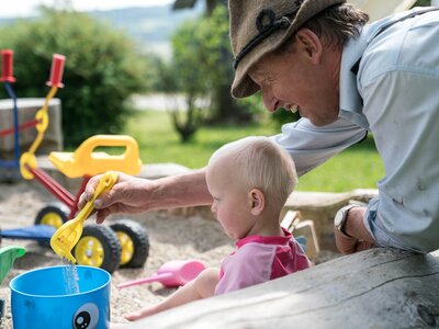Kleinkind in Sankiste | © Urlaub am Bauernhof im SalzburgerLand / Matthias Gruber Bauer spielt mit einem Kleinkind in der Sandkiste | © Urlaub am Bauernhof im SalzburgerLand / Matthias Gruber