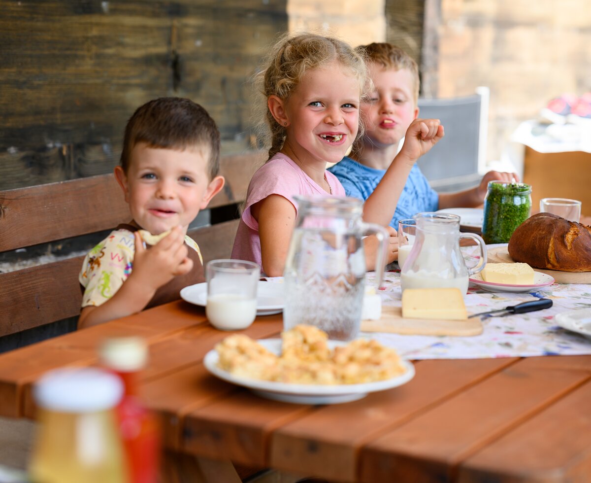 Kinder essen, jausnen am Tisch, Pausshof in Kleinarl, Salzburger Land | © Urlaub am Bauernhof / punkt&komma Ein Mädchen und zwei Jungs essen ein Jausenbrot auf der Terrasse, Pausshof in Kleinarl, Salzburger Land | © Urlaub am Bauernhof / punkt&komma