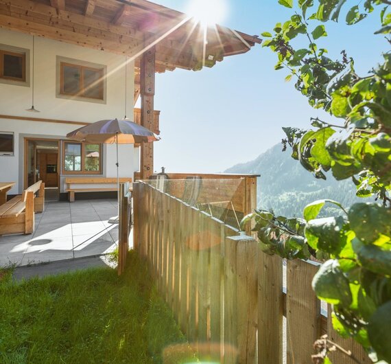 Sonnige Terrasse am Hof mit Holzbänken, Sonnenschirm und Bergblick.