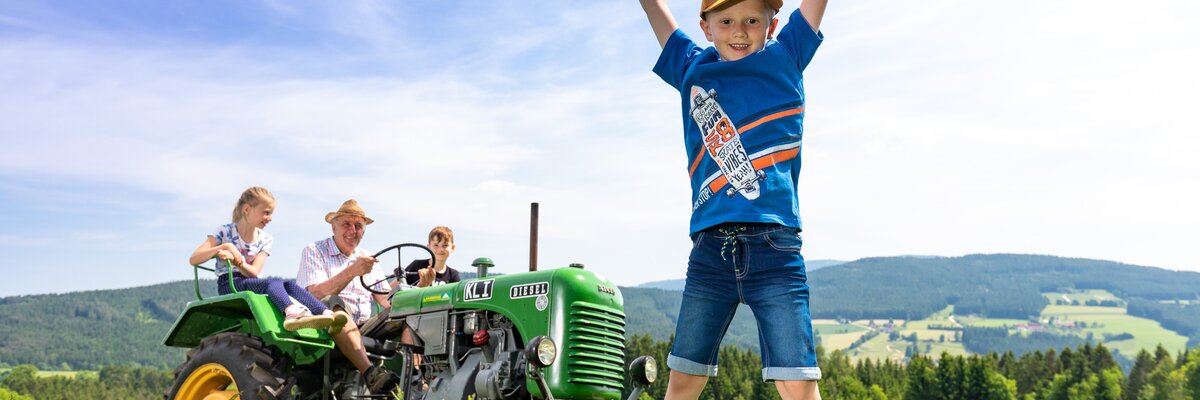 Ein Bub springt in die Luft, Traktor im Hintergrund, Steiermark | © Urlaub am Bauernhof Steiermark / Harry Schiffer