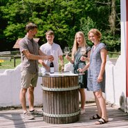 Familie Monschein mit Weingläsern am Holzfass-Tisch stehend | © Urlaub am Bauernhof Steiermark / Familie Monschein