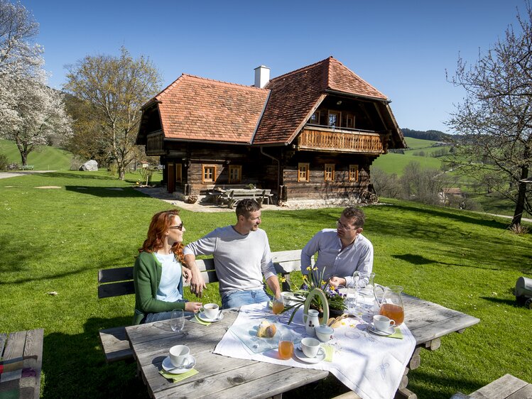 Der Bauer sitzt mit seinen Gästen beim österlich gedeckten Kaffeetisch im Freien, Steiermark | © Urlaub am Bauernhof Steiermark / Tom Lamm