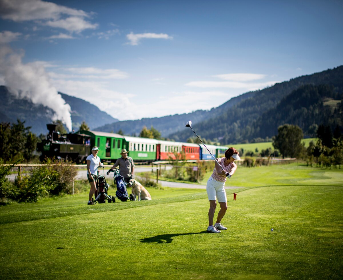 Am Golfplatz, Urlaubsregion Murtal | © Urlaubsregion Murtal / ikarus.cc Abschlag am Golfplatz mit dem Dampfbummelzug im Hintergrund, Urlaubsregion Murtal | © Urlaubsregion Murtal / ikarus.cc