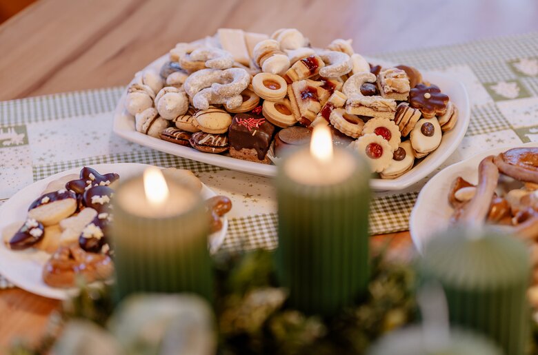 Ein volles Teller mit verschiedenen Weihnachtskeksen steht auf dem Tisch. Davor sieht man den Adventkranz, auf dem zwei Kerzen leuchten. | © UaB Steiermark / Wolfgang Spekner
